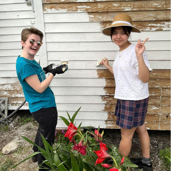 A teacher and a student smiling while painting a house on spring break